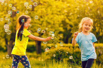 Two little girls are blowing soap bubbles, outdoor shoot.
