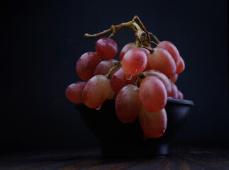 Bunch of ripe red grapes in a clay plate. Beautiful grapes on a dark background.