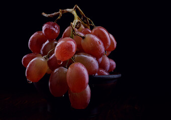 Bunch of ripe red grapes in a clay plate. Beautiful grapes on a dark background.