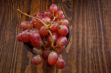 A bunch of ripe red grapes in a clay plate on a wooden table. Beautiful grapes.