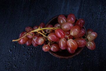 A bunch of ripe red grapes in a clay plate, on a black background with water drops.