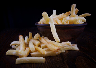 French fries in a clay cup and scattered nearby. French fries on a dark background.