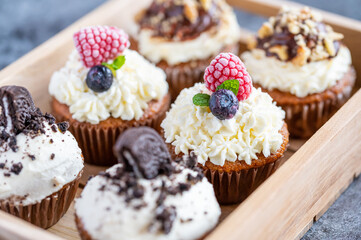 Tasty sweet muffins with mascarpone creme and chocolate, raspberry and blueberry. Fresh home baked sweets with fruit. Placed in wooden box.
