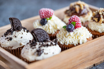 Tasty sweet muffins with mascarpone creme and chocolate, raspberry and blueberry. Fresh home baked sweets with fruit. Placed in wooden box.