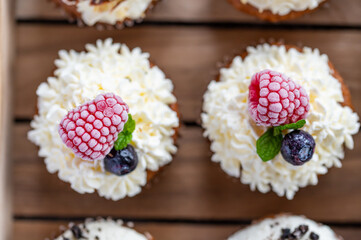 Tasty sweet muffins with mascarpone creme and chocolate, raspberry and blueberry. Fresh home baked sweets with fruit. Placed in wooden box.
