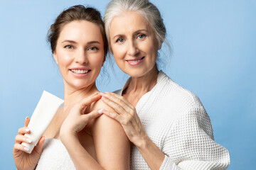 Mother and daughter holding skin cream and smiling. Two beautiful women of different ages and...