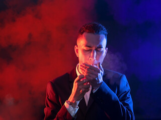 Elegant young man lighting a cigar on a black background. Selective focus