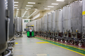 A male worker moving a bucket stainless vertical steel tanks equipment tank chemical cellar with...