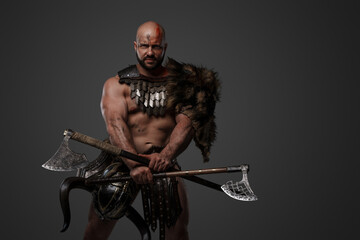 Portrait of ancient viking with fur and horned helmet holding axes in cross looking at camera.