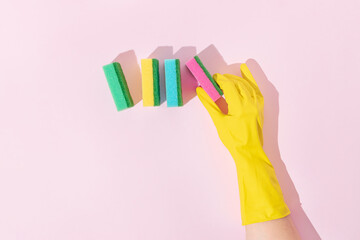 Colorful cleaning sponges and hand in yellow rubber glove trendy composition. Minimal bright pink...