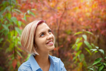 Portrait of a pensive beautiful middle-aged blonde woman, in an autumn park, on a blurred colorful autumn background of autumn foliage, sun rays break through the trees. 