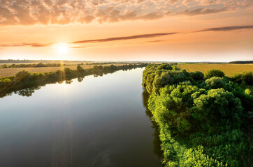 Amazing view at scenic landscape on a beautiful river and colorful sunset with reflection on water surface and glow on a background, spring season landscape