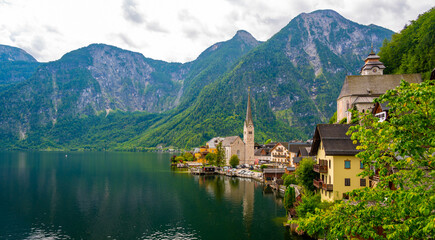 Famous view of Hallstatt city and church near the lake. Mountains in the background. Summer rainy day, soft colors, cloudy weather.