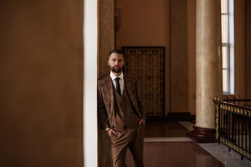 Bearded young man in a plaid jacket and a white shirt. A young guy in a stylish suit in a brown interior.