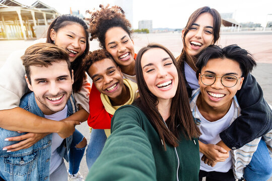 Funny young group of united multiethnic friends taking selfie portrait photo outdoors - Millennial diverse teenager people having fun laughing and celebrating together in street - Community concept