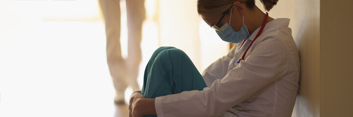 A female doctor is sitting on the floor in the hallway, close-up