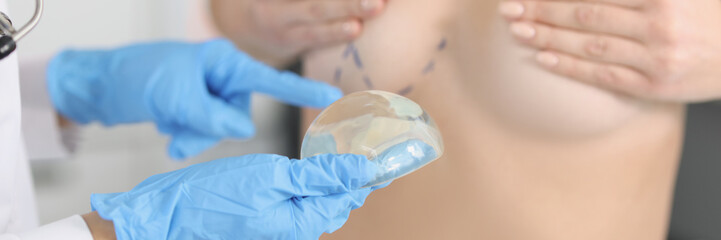 The doctor's hand holds silicone breast implant near patient
