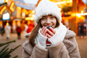Beautiful  woman in winter style clothes posing in Christmas market decorated with holiday lights.  Winter fashion, holidays, rest, travel concept.