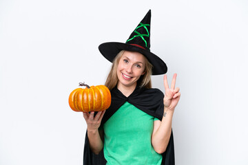 Young blonde woman dressed as a witch holding a pumpkin isolated on white background smiling and showing victory sign
