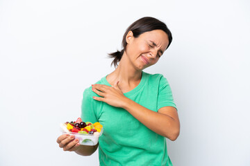 Young hispanic woman holding a bowl of fruit isolated on white background suffering from pain in shoulder for having made an effort