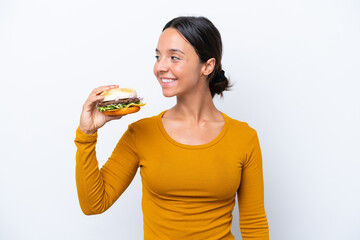 Young hispanic woman holding a burger isolated on white background looking side
