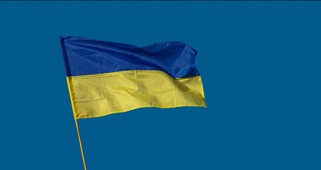 Flag of Ukraine on wooden flagpole at blue sky background. Ukrainian flag, National symbol of Ukraine in the struggle for independence, freedom and sovereignty.