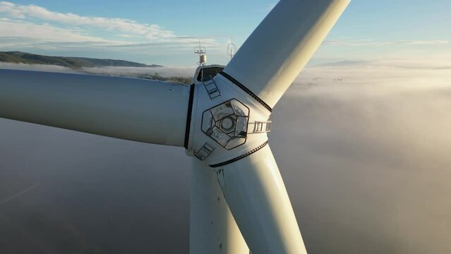 Drone shot wind turbine during sunrise dense morning fog. Close-up Wind turbines. Windmills producing clean green energy.