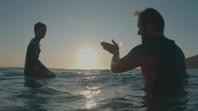 Family surfing. Father and son surfers sit in the water and father explains something to the boy - Powered by Adobe