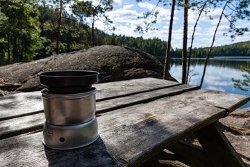 Alcohol-burning, portable stove with a lid on on the wooden table in nature with lake view in the background