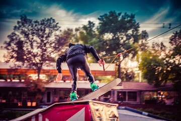 A guy in a yak suit at sunset jumps from a springboard on a wakeboard in an extreme park in Kiev....