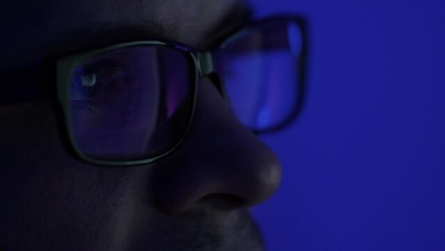 A programmer, a man in front of a computer, the code is reflected in the glasses. Working in IT, learning programming languages, developing applications and software.