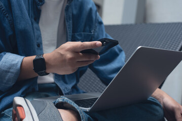 Technology and people lifestyle concept. Man freelancer sitting cross legged using mobile phone and laptop computer outdoors. Man online working and surfing the internet, close up
