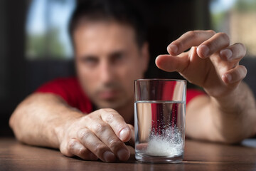 Man throwing a hangover pill into a glass of water. Effervescent tablet in water with bubbles