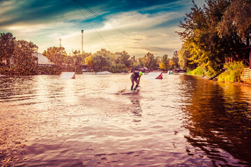 A guy in a yak suit at sunset jumps from a springboard on a wakeboard in an extreme park in Kiev....