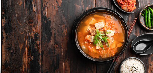 Korean food, kimchi soup with tofu in a ceramic bowl on a wooden background, top view, copy space