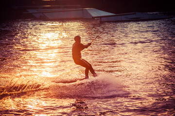 A guy in a yak suit at sunset jumps from a springboard on a wakeboard in an extreme park in Kiev....