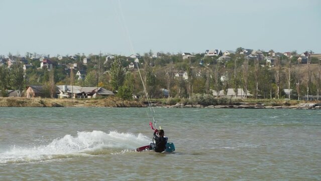 Kiteboarder rides on a kite doing and practicing tricks in sea bay. Freestyle kiter jumping, training on pond kiteboarding spot. Kitesurfer enjoying ride. Extreme water sports. Slow motion 120 fps.