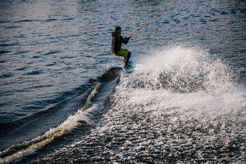 A guy in a yak suit at sunset jumps from a springboard on a wakeboard in an extreme park in Kiev....