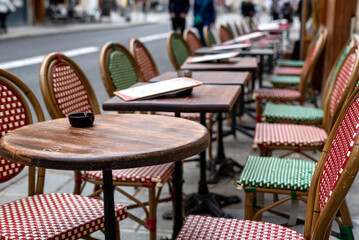 Fototapeta na wymiar Empty chairs and tables topped with a menus and ashtrays at a sidewalk in Paris, France