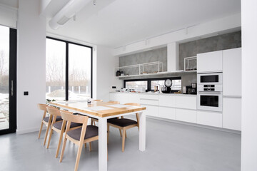 Elegant white kitchen interior with a large panoramic window without people. Stylish wooden table...