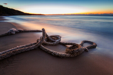 Obraz premium Scenic view of boat rope on the beach against with sky during sunrise