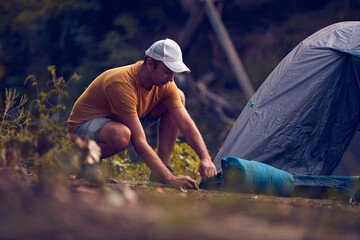 Man camping in nature, setting up the tent for overnight staying near forest river.