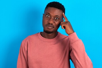 young handsome man wearing pink sweater over blue background tries to memorize something, keeps...