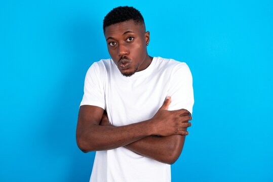 young handsome man wearing white T-shirt over blue background shaking and freezing for winter cold with sad and shock expression on face.