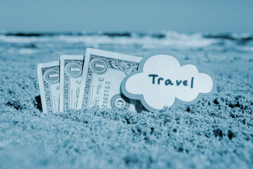 Paper bills one dollars, small stick with paper speech bubble with word Travel buried in sand beach...