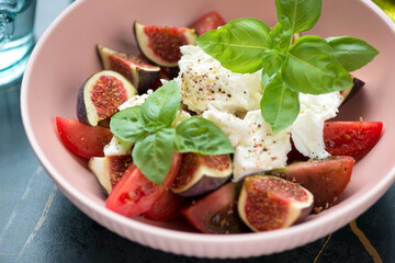 Salad with tomatoes, fresh figs, mozzarella and green basil served in a roseate bowl, close-up, selective focus