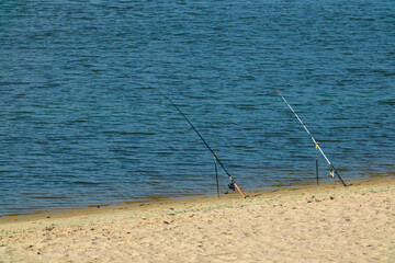Fototapeta na wymiar Fishing rods on the river bank with sandy shore on a sunny day