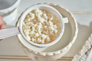 Kefir grains in a white sieve above a bowl of milk