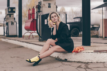 Fototapeta na wymiar Stylish blonde with make-up in a black jacket with yellow socks holds an ecological bag with bananas at the gas station.