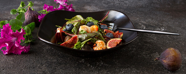 bowl with salad with shrimps, figs and blueberries on a dark table